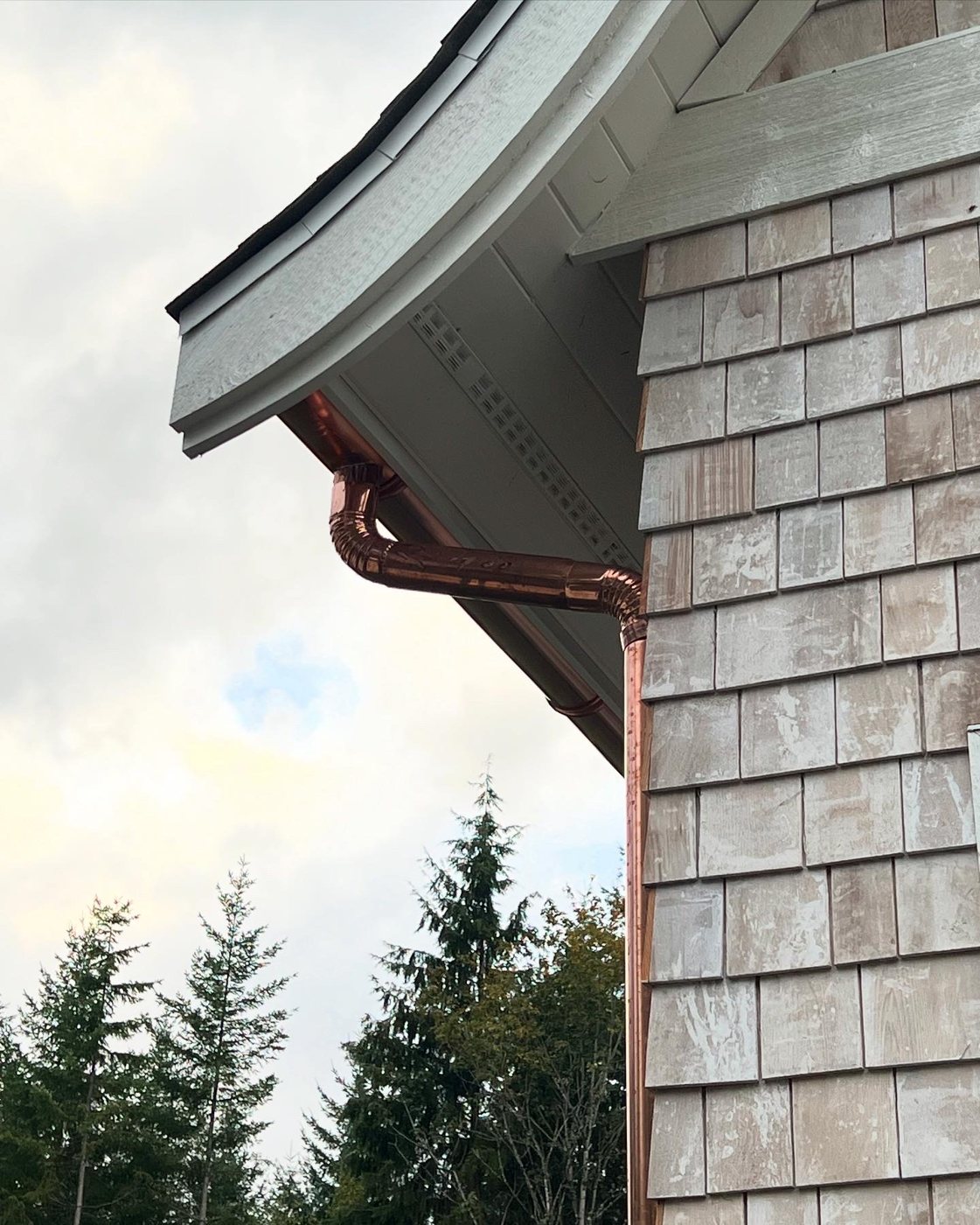 Hand-formed copper gutter and downspout detail under a curved roofline